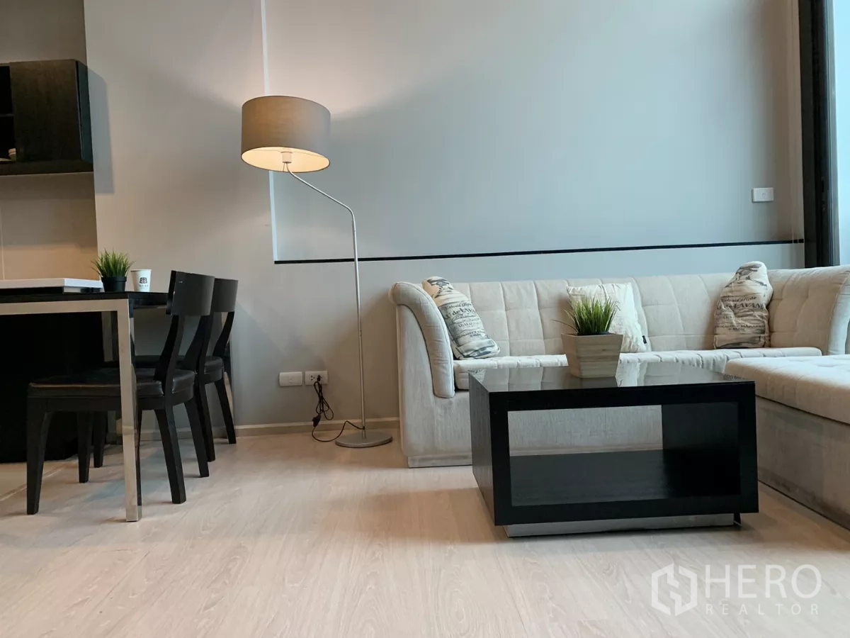 คอนโด ให้เช่าในKhlong Toei, Bangkok - มุมนั่งเล่นอบอุ่น โซฟาเข้ามุม โคมไฟยืน และโต๊ะกลางสีดำบนพื้นไม้โทนอ่อน