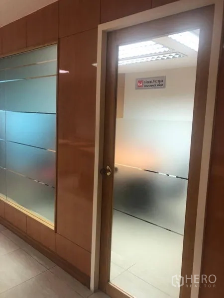 办公空间 出租在Sathon, Bangkok - 走廊旁的磨砂玻璃门与玻璃隔墙，木质墙面装饰的办公区。
