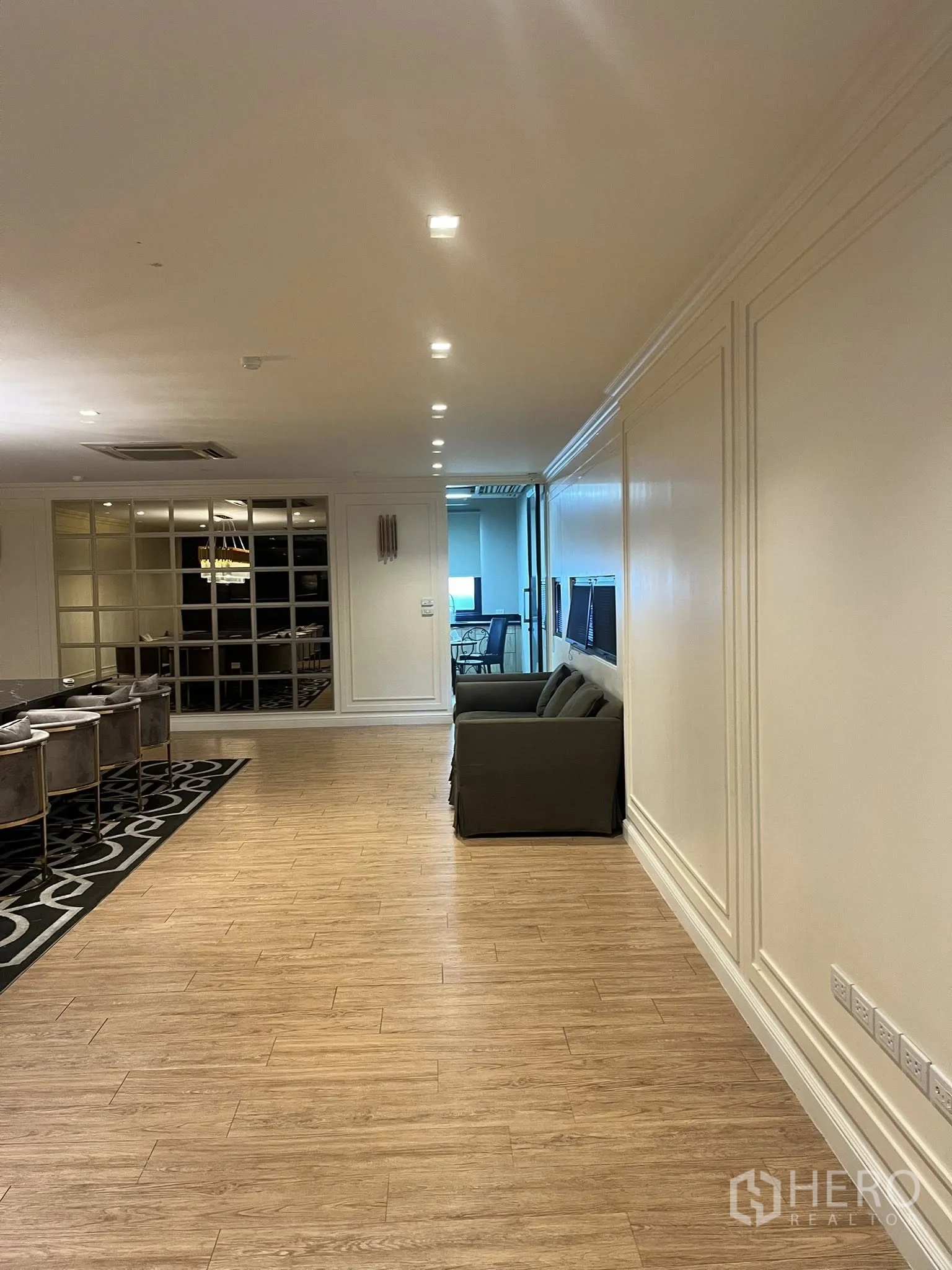 Home Office for rent in Watthana, Bangkok - Spacious lounge corridor with wood floors, sofa seating, and recessed lighting.