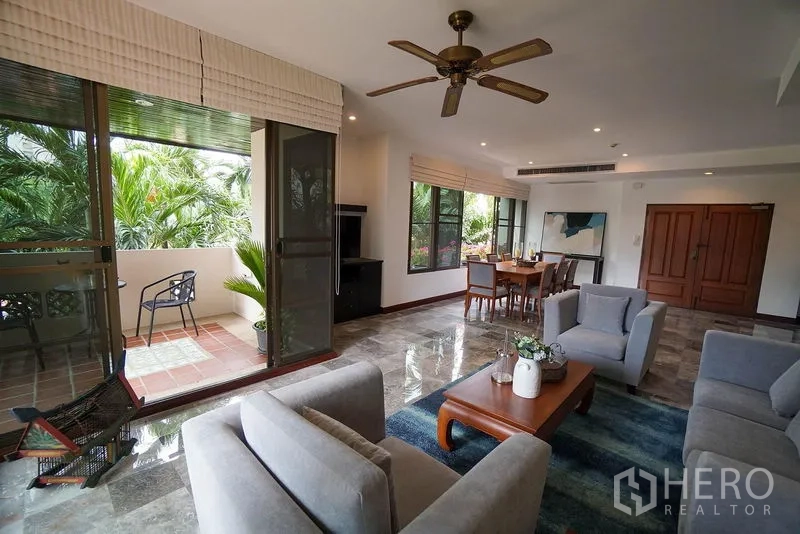 อพาร์ทเมนท์ ให้เช่าในWatthana, Bangkok - ห้องนั่งเล่นแบบโอเพ่นพร้อมโซฟาสีเทา พัดลมเพดาน พื้นหินอ่อน และประตูกระจกสไลด์ออกสู่ระเบียงร่มรื่น