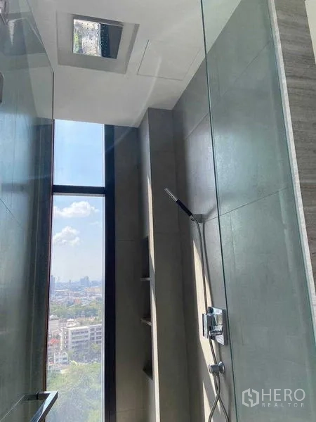 Condominium for sale in Bang Rak, Bangkok - Glass‑enclosed shower with handheld spray and tall window bringing skyline light.