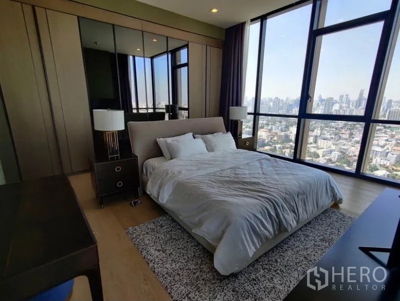 Condominium for rent in Watthana, Bangkok - Master bedroom featuring mirrored wardrobes, tall windows, and sweeping Bangkok city views.