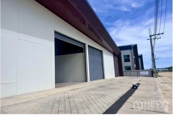 Warehouse for rent in Bang Bo, Samut Prakan - Loading area with ramped driveway and large roller shutter doors along the side of the building.