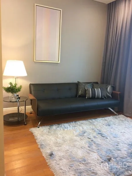 คอนโด ให้เช่าในKhlong Toei, Bangkok - มุมนั่งเล่นขนาดกะทัดรัด โซฟาสีดำ โต๊ะข้างพร้อมโคมไฟ และพรมสีอ่อน