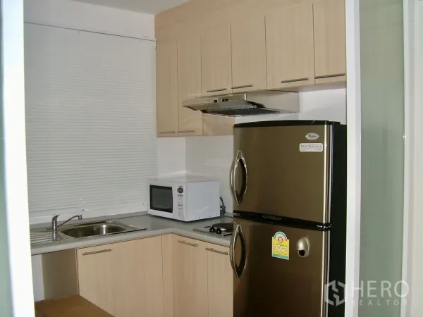 Condominium for rent or sale in Khlong Toei, Bangkok - Compact L-shaped kitchen with light wood cabinets, stainless refrigerator, hob, hood and sink.
