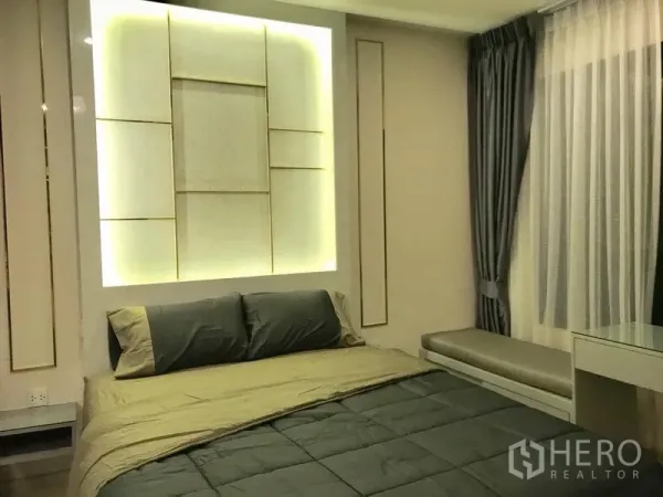 Condominium for rent in Huai Khwang, Bangkok - Cozy bedroom featuring a backlit headboard wall, bed and draped curtains.