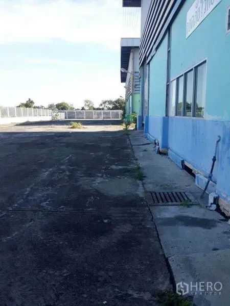 工厂 出租在Samut Prakan - 蓝色厂房侧立面与宽阔混凝土场地，带排水沟，邦沙通。