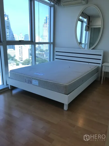 คอนโด ให้เช่าในKhlong Toei, Bangkok - ห้องนอนสว่างมีหน้าต่างสูงจรดเพดาน เตียงสีขาว กระจกเงากลม วิวเมือง