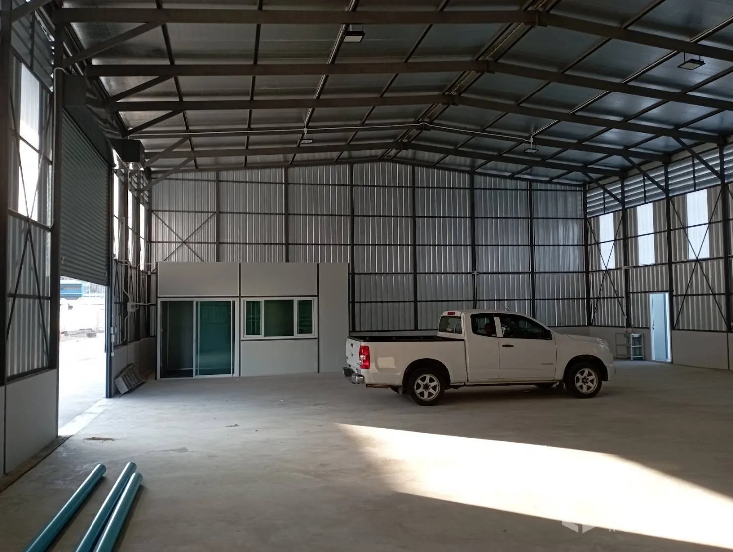 Warehouse for rent in Mueang Samut Prakan, Samut Prakan - Interior showing roller door access, office unit, concrete floor, and overhead lighting.