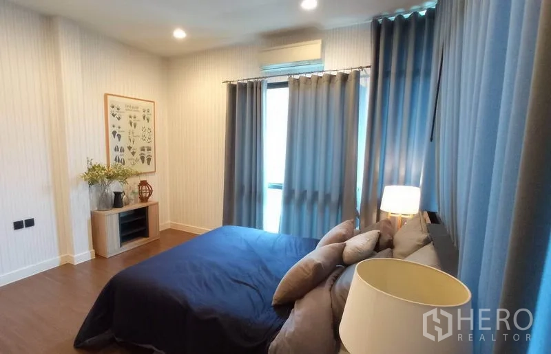 Detached House for rent in Bang Kapi, Bangkok - Secondary bedroom with wood flooring, blue curtains and soft ambient lighting.