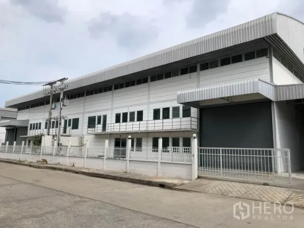 工厂 出租在Lam Luk Ka, Pathum Thani - 两层现代工厂外观，金属板立面、围栏与大型卷闸门，临安静道路
