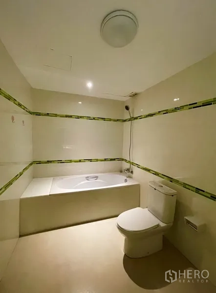 Condominium for rent or sale in Watthana, Bangkok - Bathroom featuring a built-in bathtub, handheld shower, and light tile accents.