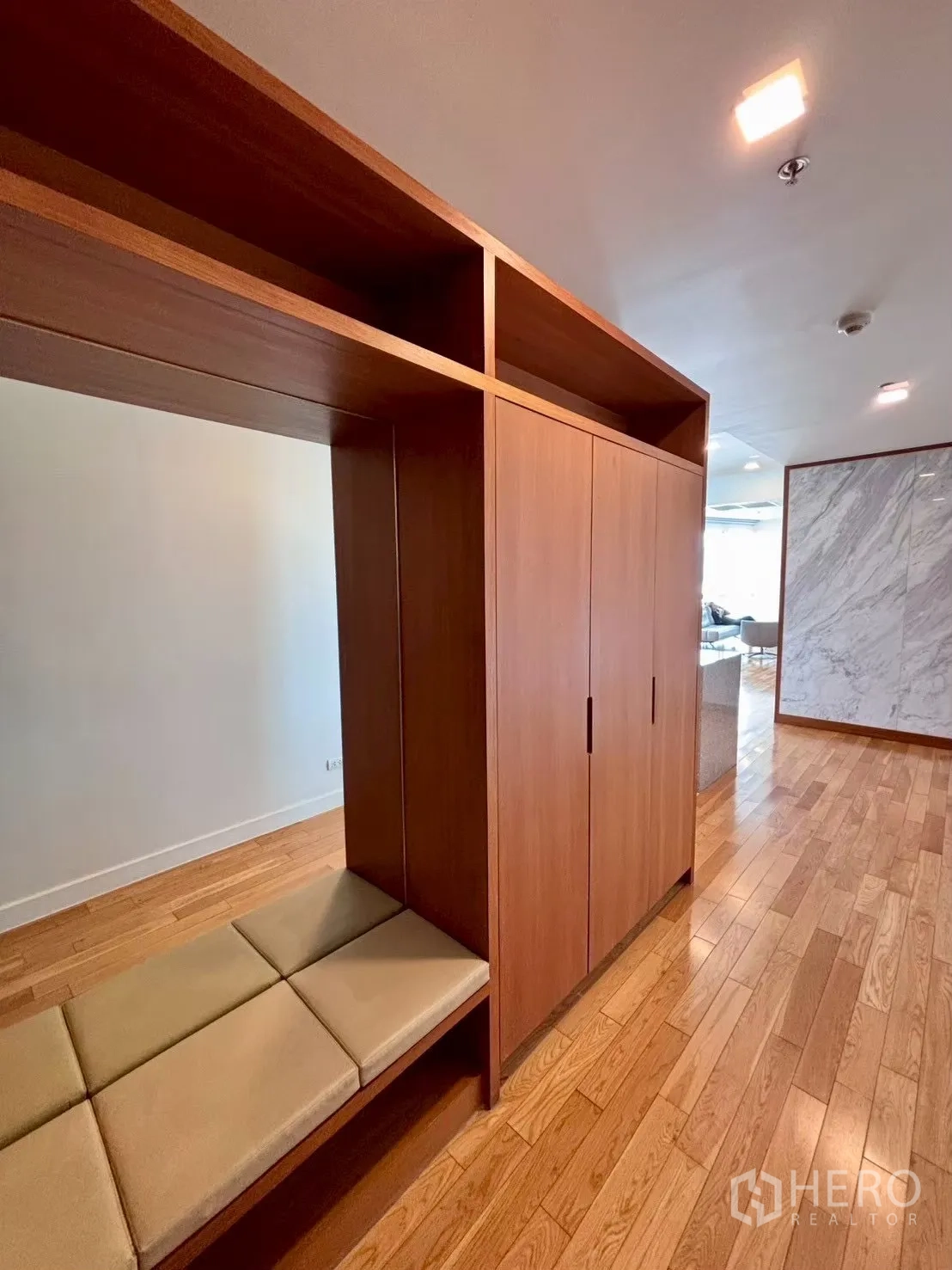 Condominium for rent in Khlong Toei, Bangkok - Entry hall with built-in wood cabinets and a cushioned bench on polished wood floors.
