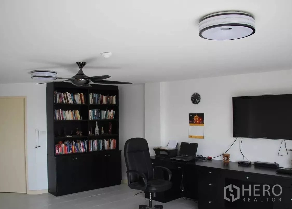 Condominium for sale in Wang Thonglang, Bangkok - Home office corner with black bookcase, ceiling fan and wall-mounted TV.