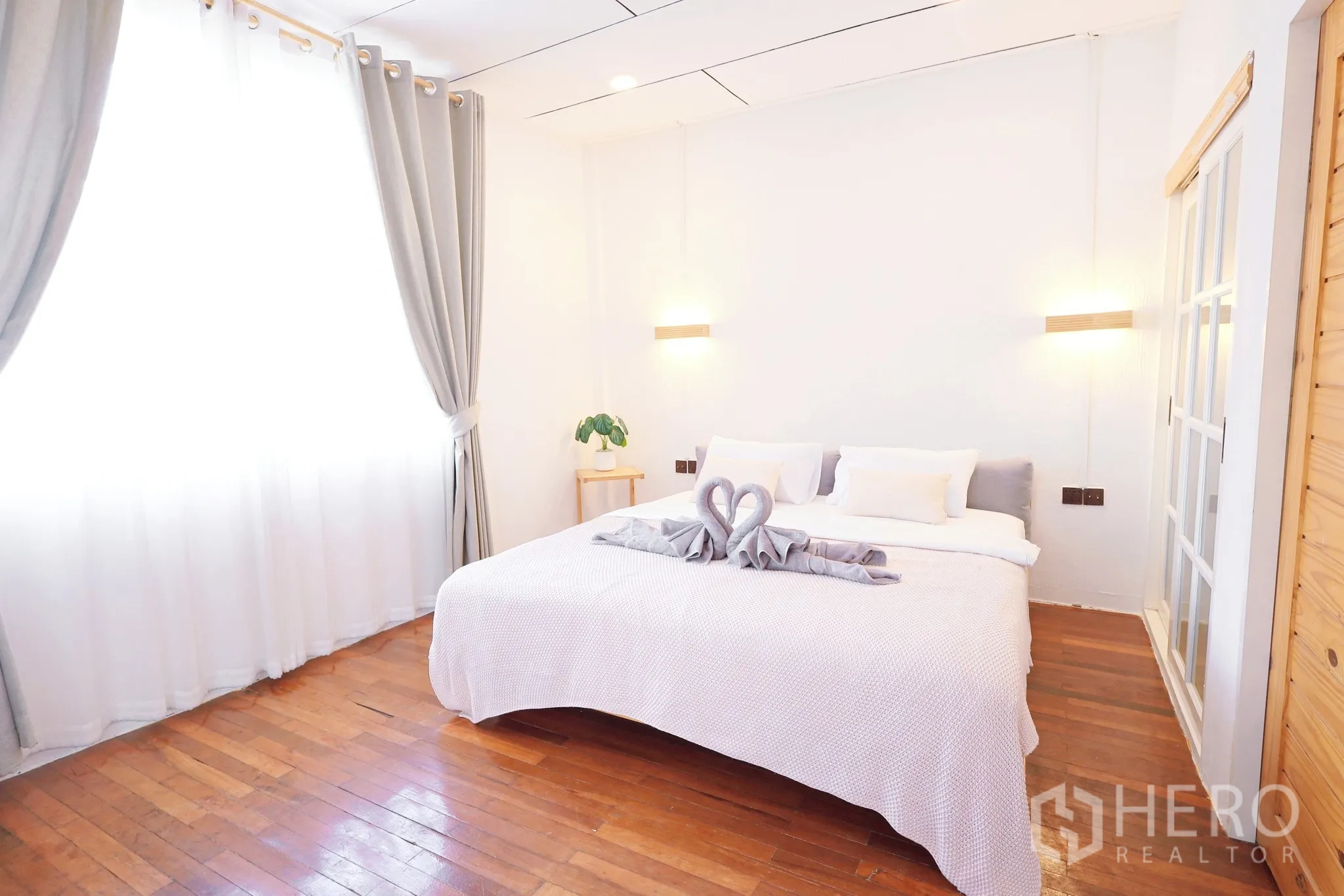 Townhouse for rent in Din Daeng, Bangkok - Master bedroom with king bed, wooden floors, soft drapes and warm wall lights.