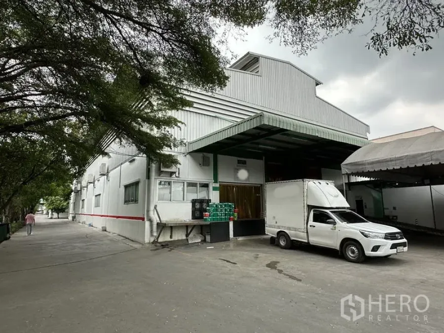 Factory for rent in Lat Krabang, Bangkok - Factory exterior with raised loading dock, metal awning and delivery truck beside shade trees.