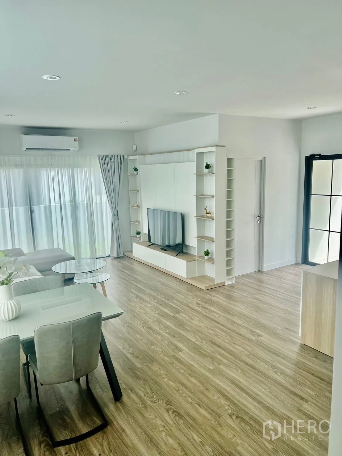 บ้าน ให้เช่าในBang Sao Thong, Samut Prakan - โซนรับแขกและทานข้าวแบบเปิดโล่ง พื้นลายไม้ ผนังทีวี และหน้าต่างผ้าม่านบานใหญ่