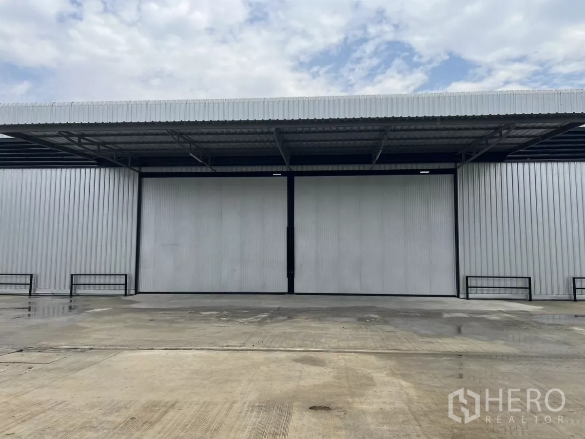 Warehouse for rent in Lat Lum Kaeo, Pathum Thani - Warehouse frontage showing a large sliding door, canopy cover, and ample maneuvering space on the concrete apron.