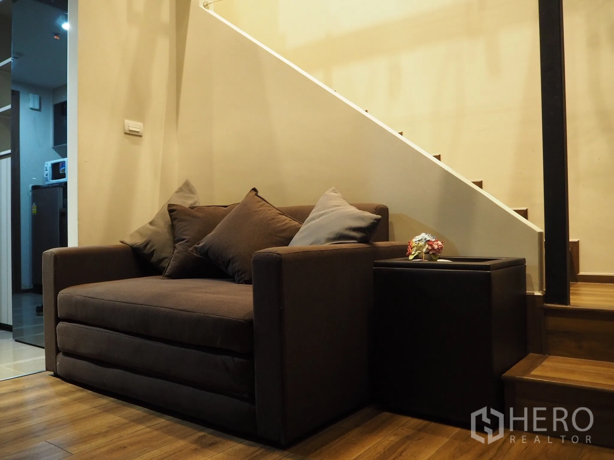 Condominium for rent in Phaya Thai, Bangkok - Cozy lounge with brown sofa beside wooden stairs in a loft-style condo.
