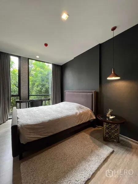 คอนโด ให้เช่าในWatthana, Bangkok - ห้องนอนโทนเข้มพร้อมผนังเน้น โคมไฟห้อย และหน้าต่างสูงเต็มบานมองเห็นต้นไม้เขียว