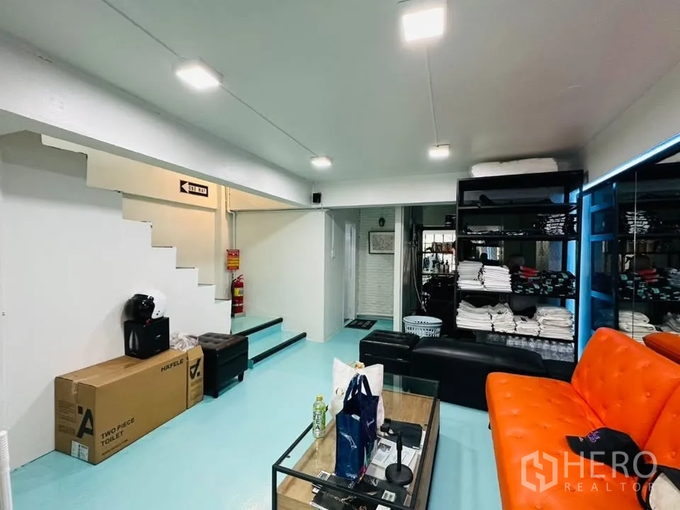 店屋 for sale in Watthana, Bangkok - 休息与储物区，橙色沙发、置物架及室内楼梯。