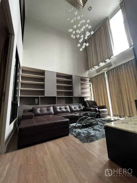 ทาวน์เฮาส์ ให้เช่าในKhlong Toei, Bangkok - พื้นที่นั่งเล่นเพดานสูง โซฟาสีเข้ม ชั้นวางหนังสือ และผ้าม่านสูง