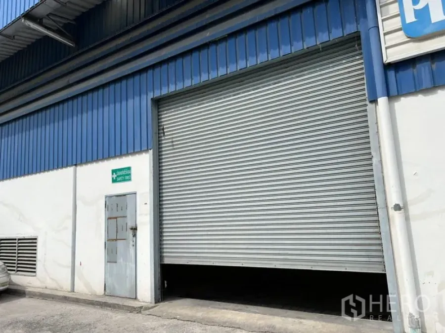 Warehouse for rent in Suan Luang, Bangkok - Exterior of the warehouse with a large metal roller shutter loading door and blue cladding.