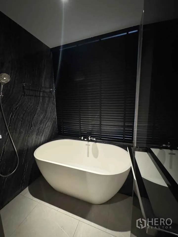 Condominium for rent in Watthana, Bangkok - Modern bathroom with freestanding bathtub beside dark stone wall.