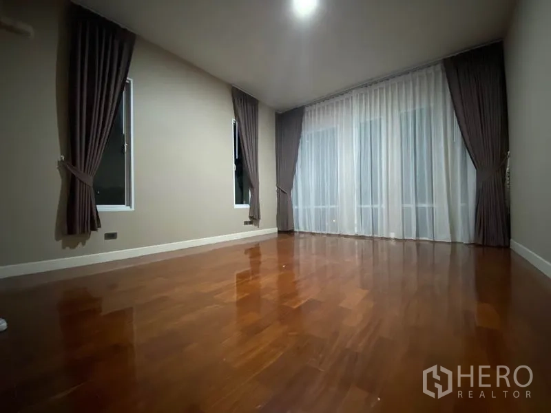 Detached House for rent in Prawet, Bangkok - Large bedroom with wooden flooring, full-height curtains and corner windows.