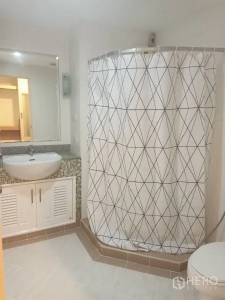 Condominium for rent or sale in Watthana, Bangkok - Clean bathroom with vanity and large mirror, tiled floor and shower area with patterned curtain.