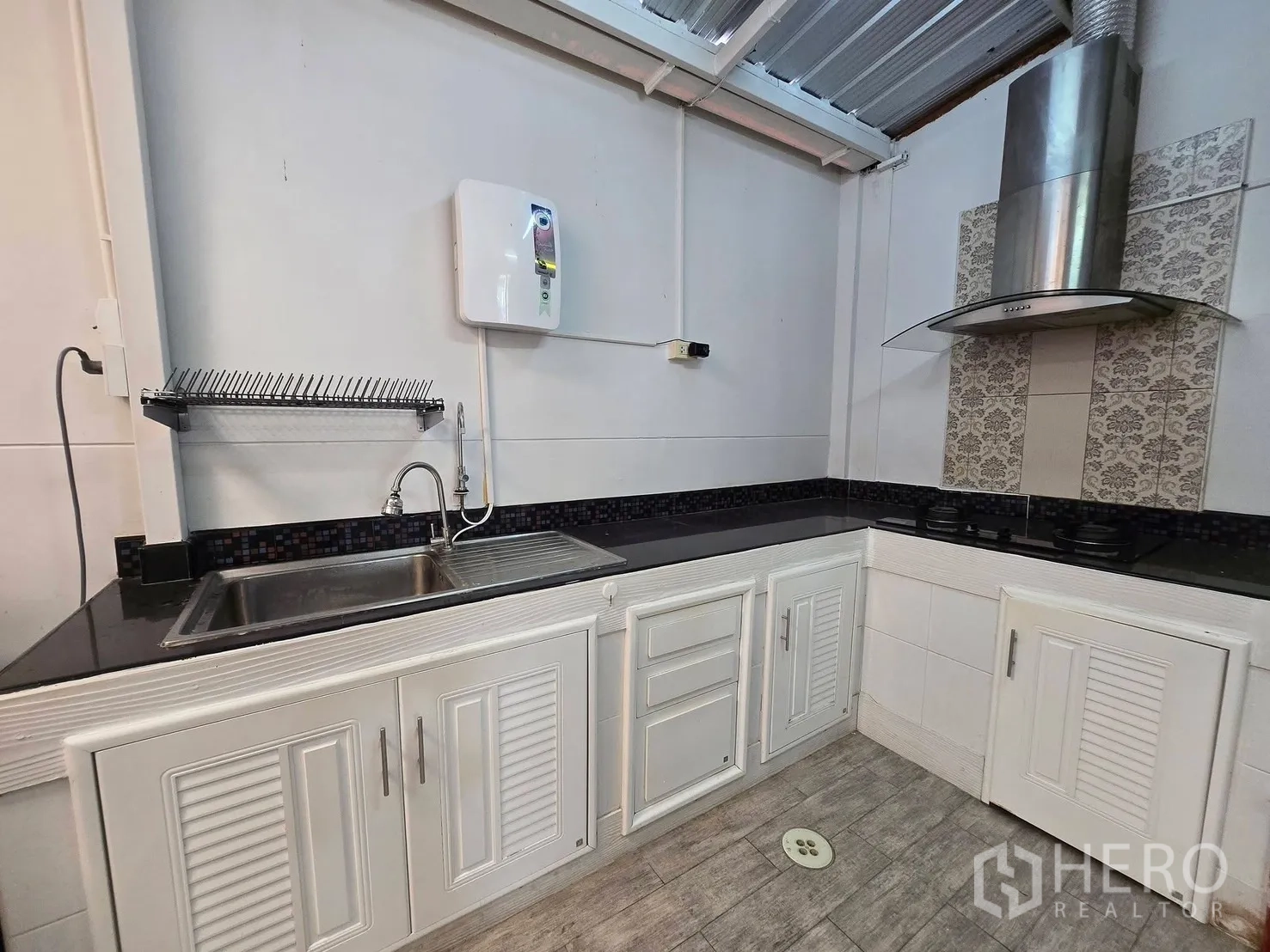 Townhouse for rent in Bang Phli, Samut Prakan - Practical rear kitchen with white cabinetry, black countertops, gas hob and hood.