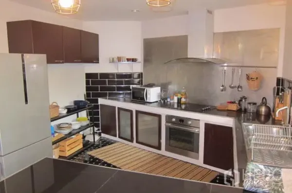 Townhouse for rent in Khlong Toei, Bangkok - Modern kitchen with L-shaped counters, black subway tiles, oven and stainless range hood.