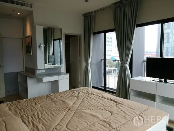 Condominium for rent in Watthana, Bangkok - Master bedroom featuring a dressing vanity, sliding glass doors to the balcony, TV console and tall curtains with abundant natural light.
