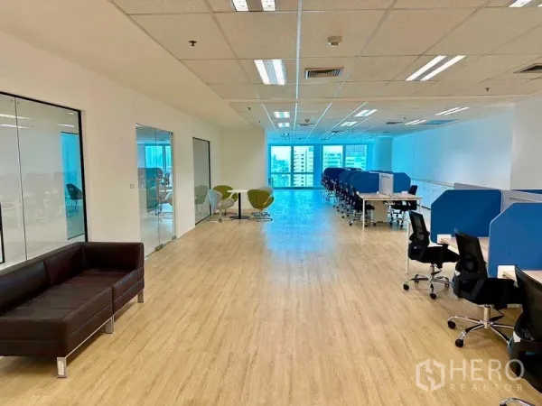 Office Space for rent - Long office layout with sofa lounge, glass meeting rooms and rows of partitioned desks under ample natural light.