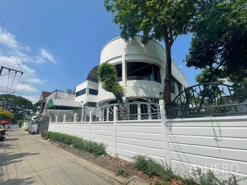 Home Office for sale - Street view of curved modern facade behind a high white perimeter fence and mature trees.
