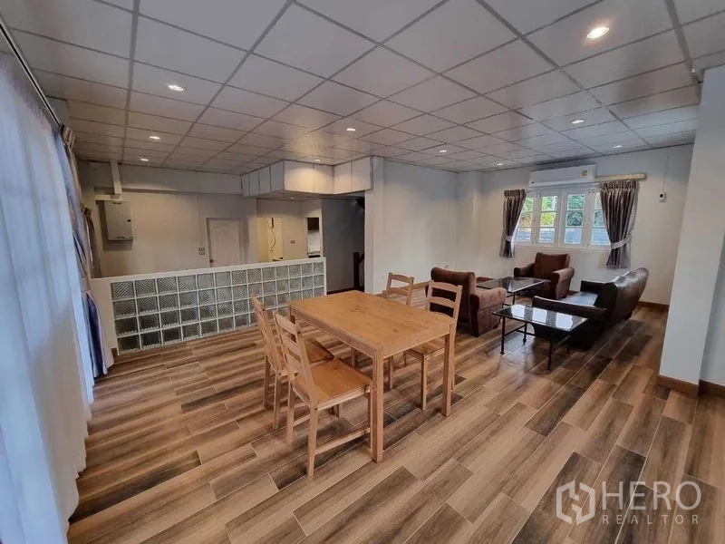 独立式住宅 出租在Mueang Nonthaburi, Nonthaburi - 餐区配木质餐桌，邻玻璃砖隔墙与大幅窗帘。