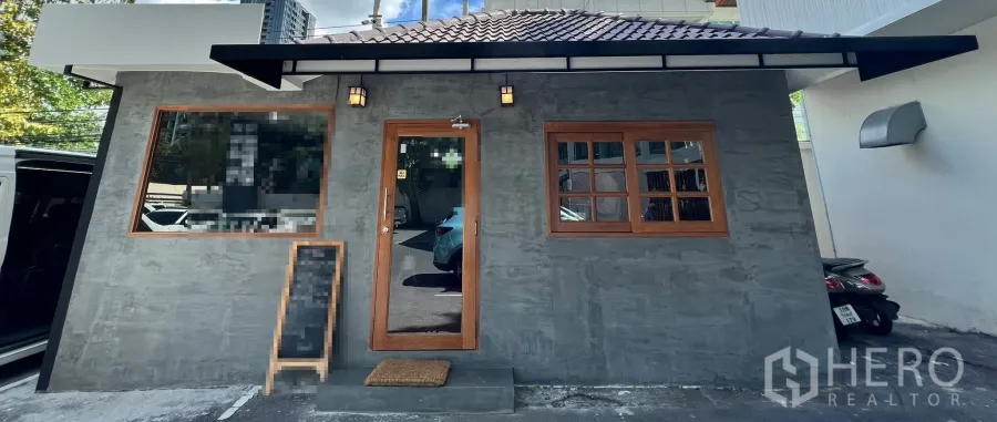 零售空间 出租在Watthana, Bangkok - 已翻新的一层零售铺面，灰色外墙与木框门窗，带雨棚及停车位，曼谷瓦他那区。