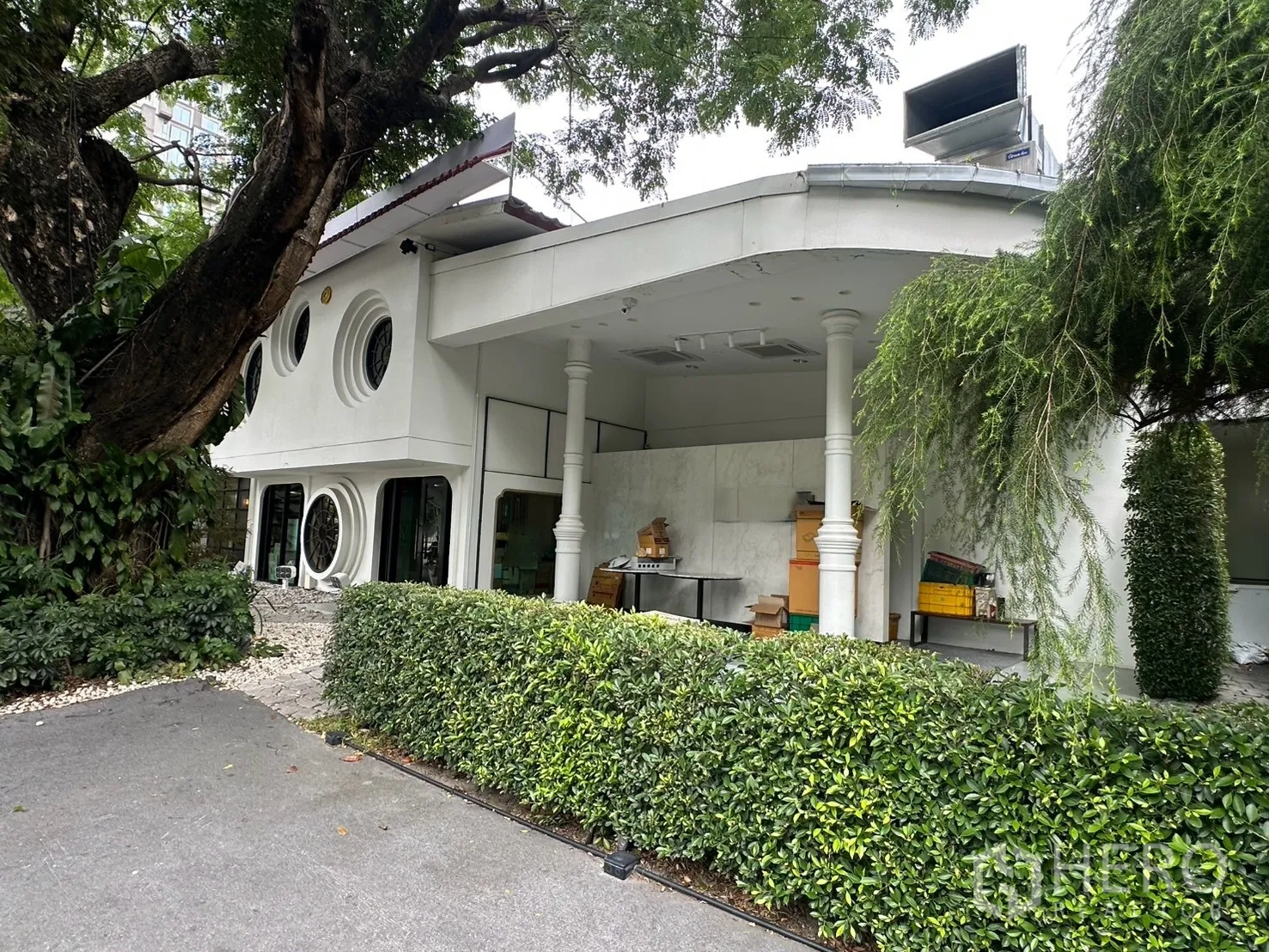Detached House for rent in Watthana, Bangkok - Exterior side view of the house with columns and mature trees.