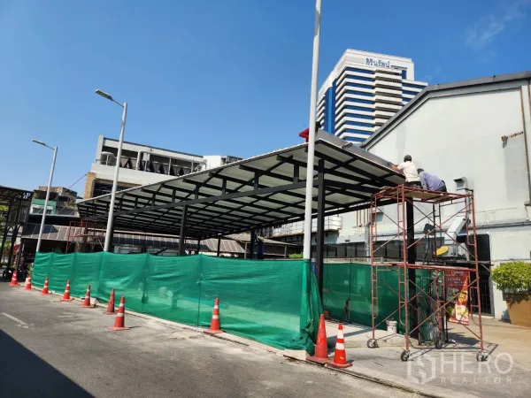 零售空间 出租在Khlong Toei, Bangkok - 道路侧视图，钢结构雨棚商铺配脚手架与绿色围挡，位于曼谷商务区。