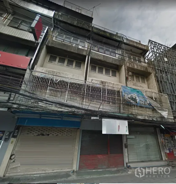 Shophouse for rent in Khlong Toei, Bangkok - Four-storey Bangkok shophouse facade with balconies, metal grilles and closed roller shutters on a busy street.