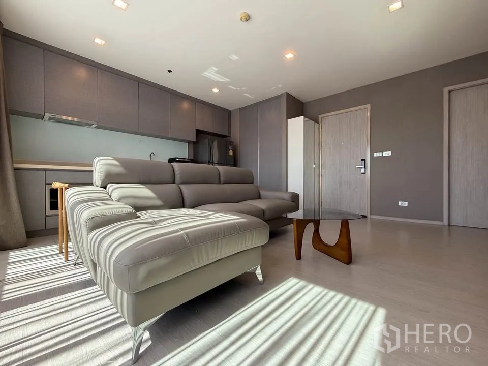 Condominium for rent in Khlong Toei, Bangkok - Bright lounge with sectional sofa, coffee table and full-length kitchen cabinetry.