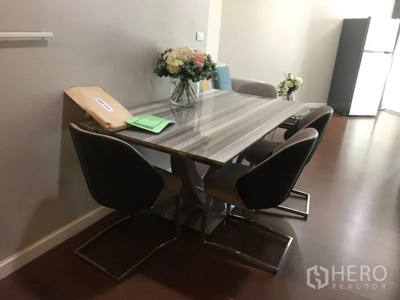 Condominium for rent or sale in Huai Khwang, Bangkok - Dining area with marble-top table, four modern chairs and vase of flowers on wood flooring.
