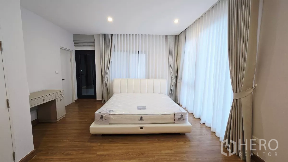 Detached House for rent in Prawet, Bangkok - Bright ensuite bedroom with desk and wraparound curtains.