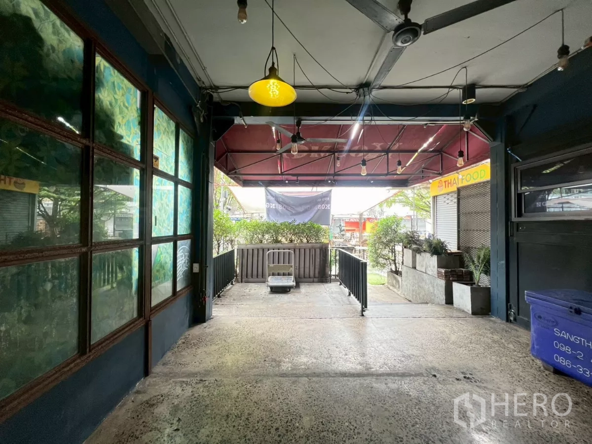 零售空间 出租 - 带顶棚的门廊，串灯、花箱与护栏，面向步行区。