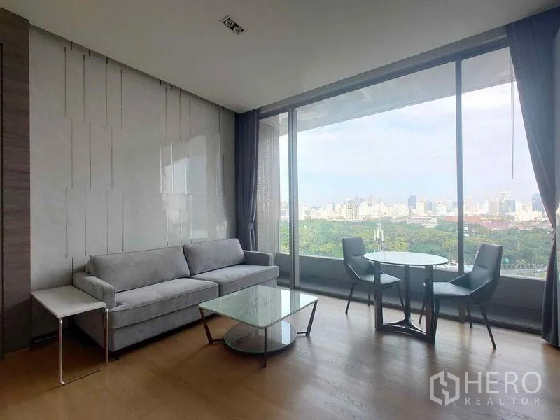 公寓 出租在Bang Rak, Bangkok - 现代客厅，灰色沙发、玻璃茶几和圆形餐桌，旁有全景落地窗与城市景观。