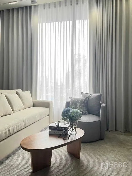 คอนโด ให้เช่าในKhlong San, Bangkok - มุมพักผ่อนสว่าง โซฟา เก้าอี้อาร์มแชร์ และโต๊ะกลาง ข้างผ้าม่านโปร่งกับวิวสกายไลน์เมือง