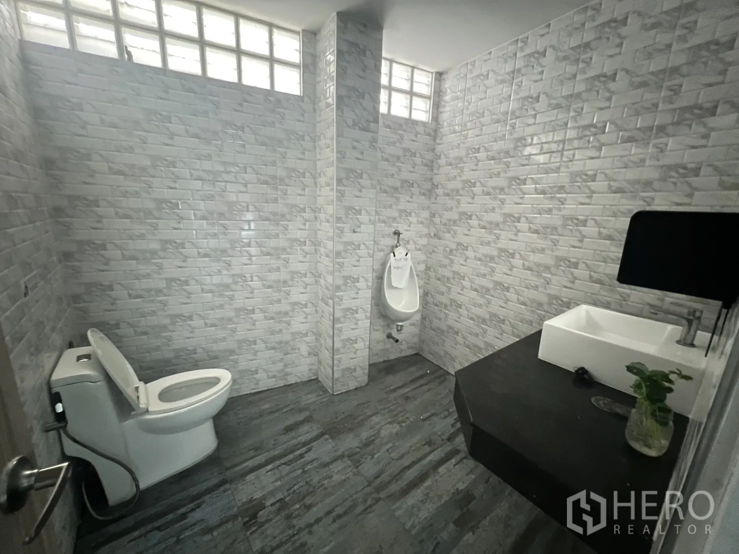 零售空间 出租在Khlong Toei, Bangkok - 翻新卫浴，灰白瓷砖墙，坐便器、尿斗与洗手盆。