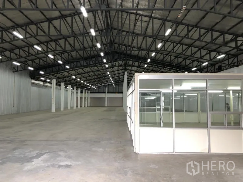 货栈 出租在Nonthaburi - 带玻璃办公室区块的仓库大厅，光线均匀，混凝土地坪平整。