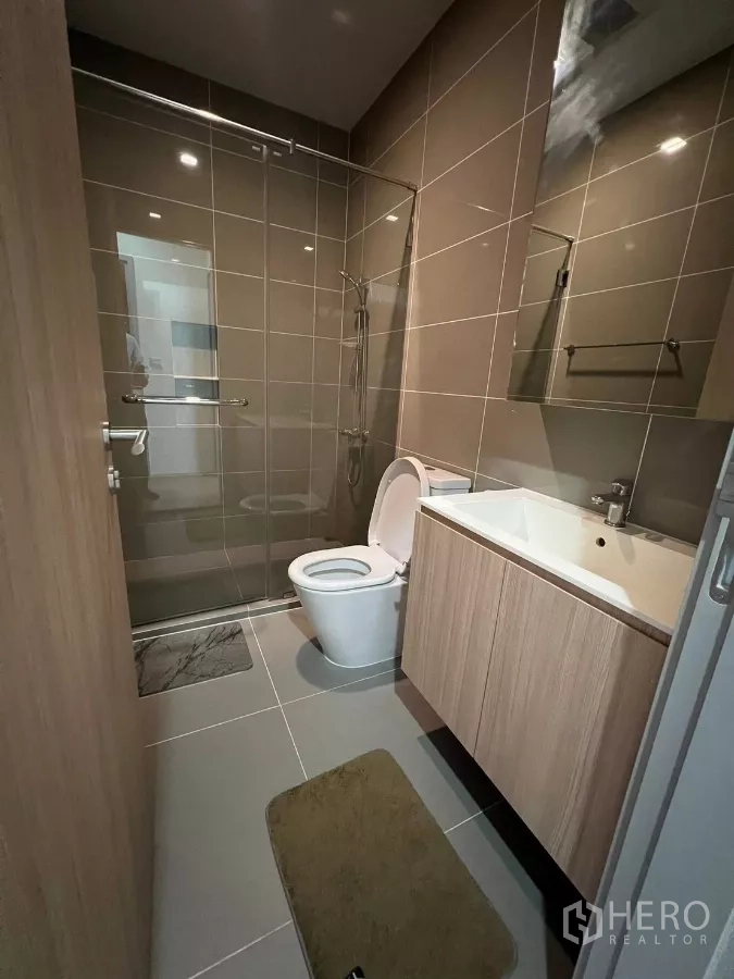 公寓 出租或出售在Chatuchak, Bangkok - 浴室设玻璃淋浴间、洗手台与马桶，色调中性。