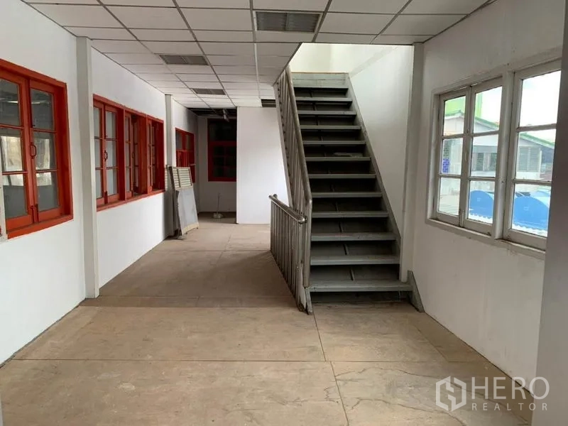 Warehouse for rent in Suan Luang, Bangkok - Office corridor with multiple windows and a metal staircase beneath a suspended ceiling.